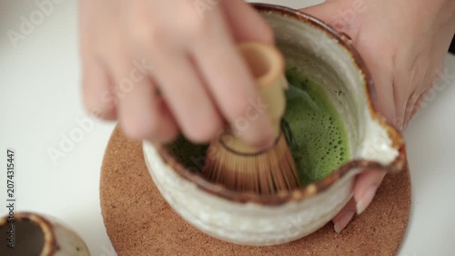 Close up woman's hand making traditional green tea matcha using bamboo natural whisk mixing beverage for healthy drink with antioxidant nutrition in wellness routine and modern healthy lifestyle.
