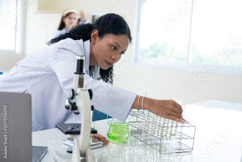 African American female scientist working with microscope and notebook computer in laboratory