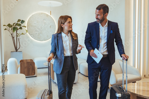 Business Professionals Walking Through Hotel Lobby With Luggage Discussing Travel Plans During Corporate Trip