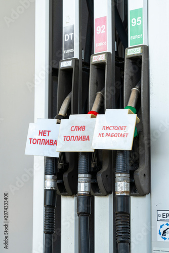 Fuel nozzles at a gas station pump with signs reading: no fuel, fuel drain, and nozzle not working. No gasoline available.