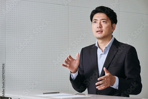 Foto 相手の目を見てデスクでプレゼンを行いながら話す30代の日本人の男性の会社員