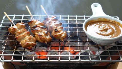 Delicious Chicken Satay Skewers Grilling on Charcoal with Rich Peanut Sauce Served in a Bowl on Table