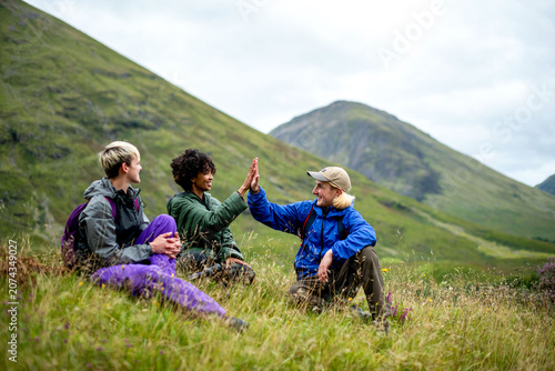 Valokuva Three friends high-five while sitting on a grassy hillside outdoors
