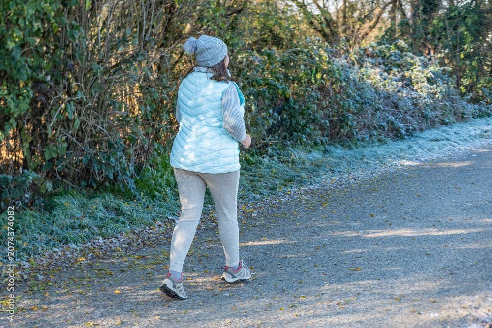 Fototapeta premium away from the camera on frosty park path early in morning, back view active lifestyle and healthy aging sports in nature during cold weather, winter jogging motivation, healthier routine in nature