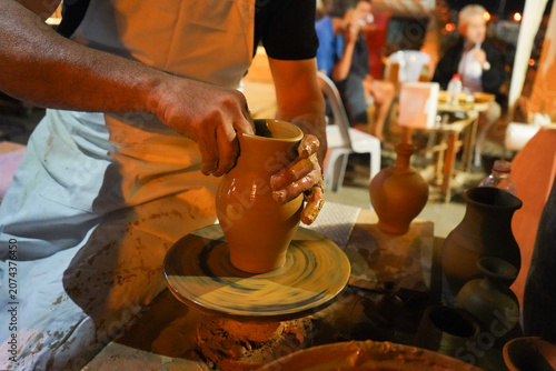 Close-up of an artisan's hands shaping a clay vase on a pottery wheel under warm, low-light artificial illumination in Crete.