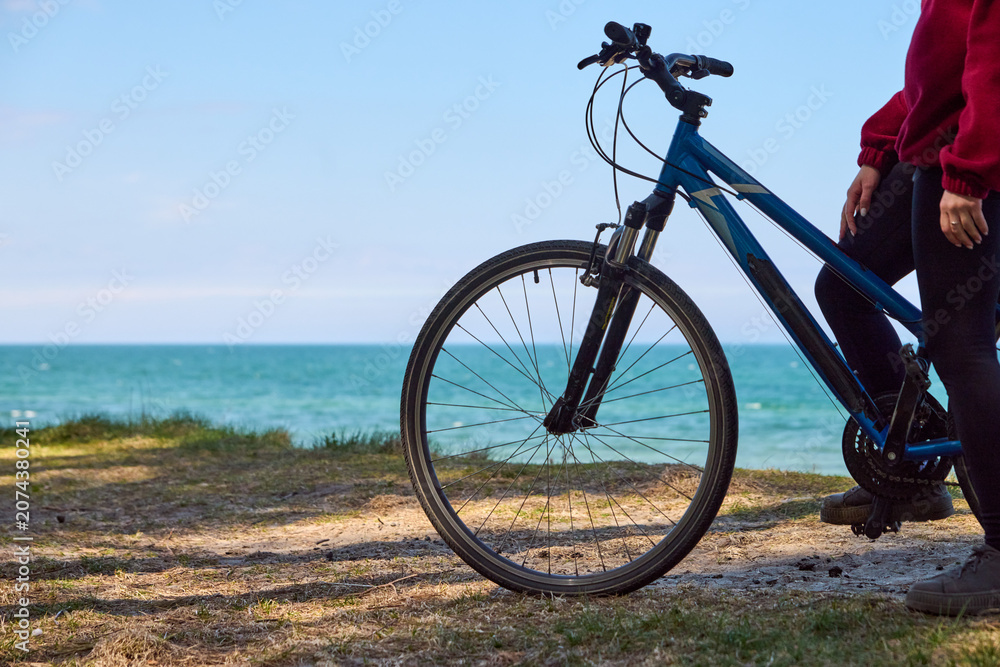 Fototapeta premium Young adult person standing with blue bicycle near ocean shore under clear sky