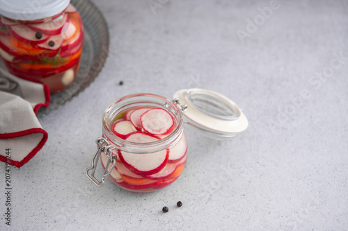 Homemade pickled radish in a glass jar on a light kitchen table