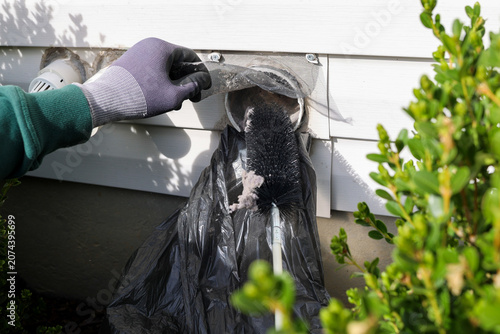 A man cleaning a outdoors dryer lint  vent