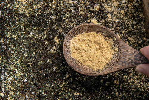 Dried ginger powder Zingiber officinale is mainly used as a natural aid for pest control and plant support in the garden. Hand holding spoon and scattering ginger powder in greenhouse.