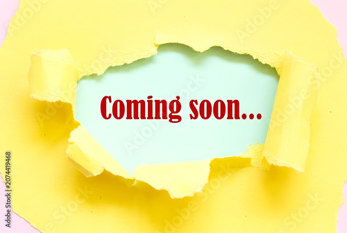 Coming Soon Message Revealed Through Torn light yellow Paper For Product Launch Marketing Announcement And Business Promotion Concept