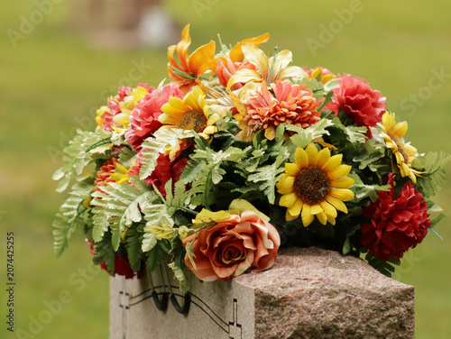 Konstfotografi Pink, orange and yellow artificial flowers laid atop a headstone in a historic c