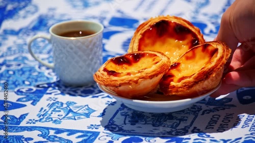 Plate of Pastel de Nata tarts served by hand near coffee cup on blue