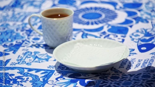 A hand picking and placing a pastel de nata on white saucer on blue