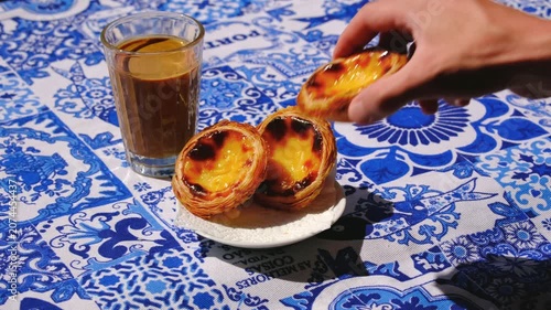 Hand taking one pastel de nata custard tart from a serving on azulejo