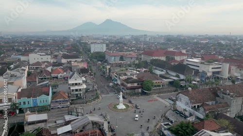 Drone footage of Tugu Yogyakarta, an iconic historic landmark located in the heart of Yogyakarta, Indonesia. Aerial view captures the striking white monument standing prominently at a busy city inters