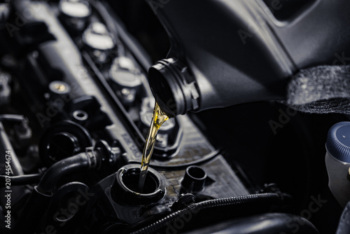 Photos close-up of pouring engine oil from a bottle into a car's engine compartment