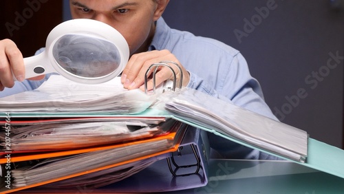 Vászonkép Man holding a magnifying glass, intently reviewing financial documents and binde