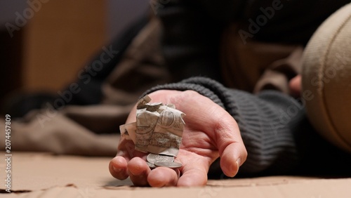 Obraz na płótnie Person experiencing homelessness is lying on a cardboard surface, reaching out h