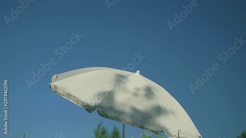 Relaxes under a white umbrella enjoying a sunny day. The blue sky overhead highlights the joyful atmosphere of summer. The setting invites relaxation and simple enjoyment.