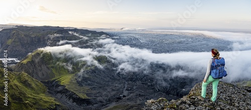 Hiker looks over spectacular landscape, mist on cliffs and glacier Myrdalsjökull, Pakgil, Iceland