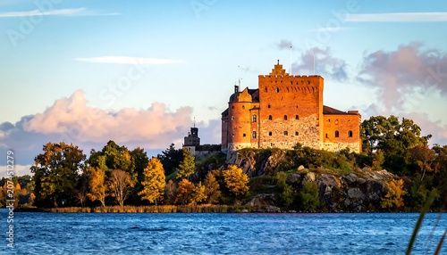 Historic Brick Castle Glowing in Golden Sunset Light on Rocky Island Shoreline