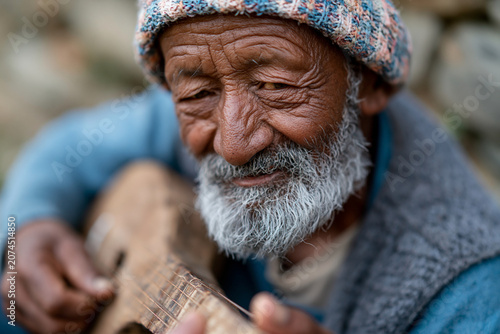 Warm smile lights up an elderly man's face. His weathered hands strum a simple wooden instrument. Colorful knit cap adds character to his rugged look. Soft focus background suggests a quiet