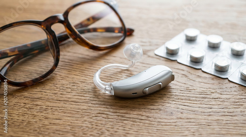 Close-up of a hearing aid beside eyeglasses and medication, symbolizing aging, hearing loss, and elderly healthcare support in everyday life.