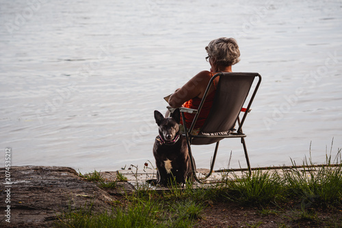 Peaceful senior woman relaxing by the water with her loyal black dog