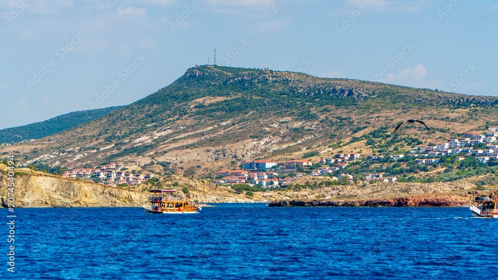 Fototapeta premium Izmir, Turkey - June 21, 2026: Scenic nature view near Foça, featuring Mediterranean vegetation, rocky coastline, green hills, blue Aegean Sea, calm water, and natural coastal landscape.