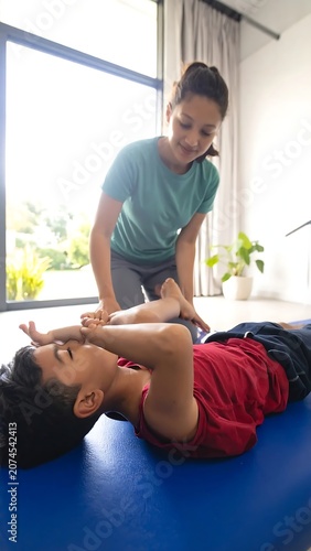 Caring Young Woman Assisting Child Stretching on Exercise Mat in Bright Living Room