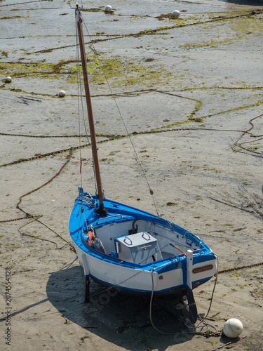 blau-weißes Segelboot, welches bei Ebbe im Hafen liegen geblieben ist