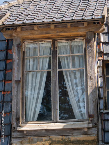 Aussenaufnahme eines alten Holzfensters mit weißen Gardinen