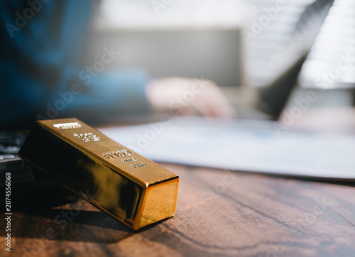 Gold investment concept. Gold bar on office desk with financial report for wealth management, asset protection, market analysis, and economic security.
