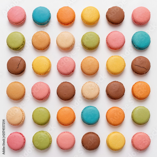 Symmetrical 6x6 arrangement of colorful macarons in a perfect checkerboard pattern on a clean white background, featuring minimalist luxury food styling in an overhead studio composition.