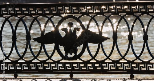 picturesque metal railings with a double-headed eagle and the crown of the Russian Empire on embankment in St. Petersburg, Russia, walking people, sunny autumn day, incredible sun glare Russia