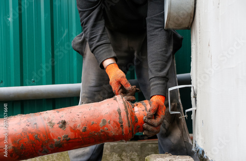 Plumber installing orange plastic sewage pipe outdoor. Worker in gloves fixing sewer pipeline system, drainage installation, construction or renovation utility repair service