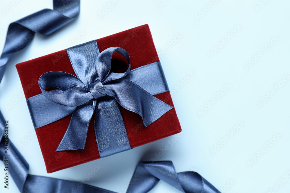 Fototapeta premium Beautiful velvet gift box and ribbon on light blue background, flat lay. Space for text