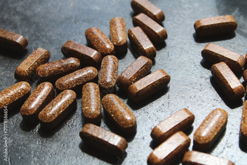 Tableau sur toile Close-up of scattered brown herbal supplements on a dark textured surface, featuring natural lighting and harsh shadows for a wellness and health concept