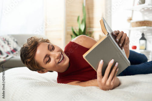 Φωτογραφία A joyful young woman enjoys a quiet moment at home, immersed in a good book while lying on her bed