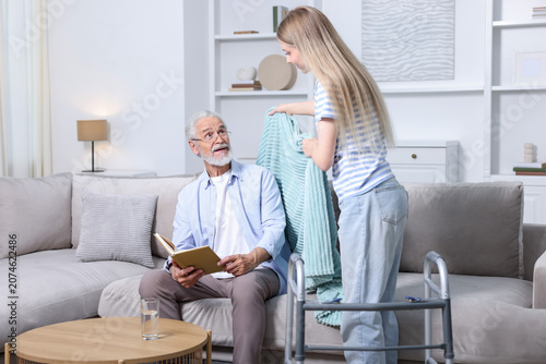 Foto Caregiver. Teenage girl taking care of elderly man indoors