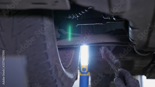 An auto mechanic is working under a car on a car lift in a garage. The auto repair shop provides auto repairs. The repair of the bottom of a car is done in a modern auto repair shop.