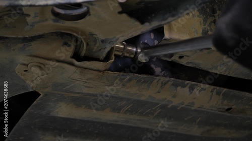 A mechanic works under a car in a garage on a car lift. The mechanic is repairing the bottom of the vehicle in a modern automotive repair shop.