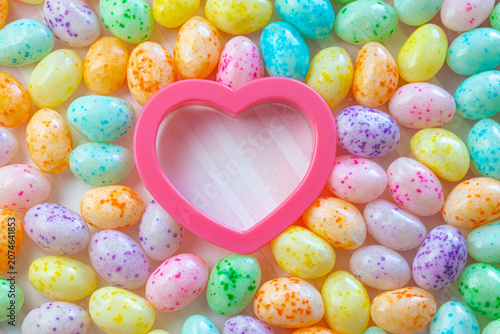 Colorful Speckled Jelly Beans Surrounding a Pink Heart on a Pink Striped Background