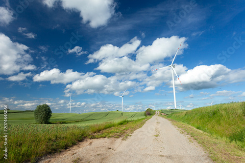 Wind turbines standing in a green field with a road and a clear sky