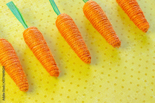 Yarn Woven Orange Carrots in a Row on a Yellow Spotted Background