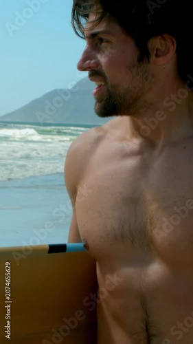 Vertical video: Seeing waves, shirtless surfer holding yellow board in red trunks preparing to surf