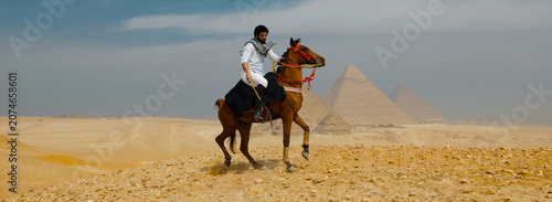Canvas Print Heroic Arab horseman in white shirt and keffiyeh galloping a brown horse across