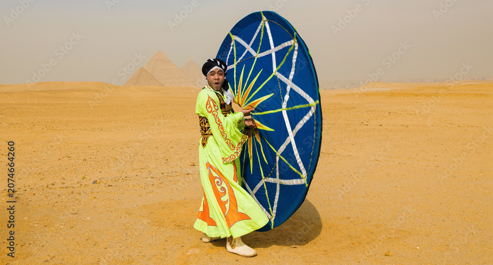 Fototapeta premium Theatrical folk dancer in colorful green costume performing a dynamic spinning skirt dance pose in the desert near the Giza pyramids ideal for