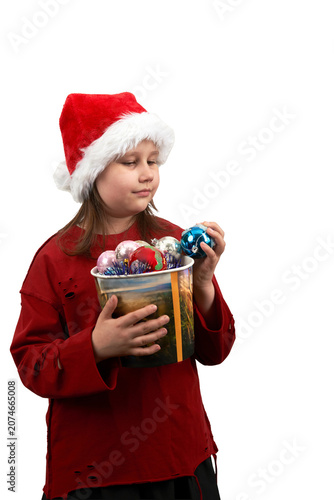 A primary school-aged girl wearing a Santa Claus hat holds a popcorn bucket filled with colorful Christmas tree baubles. PNG.