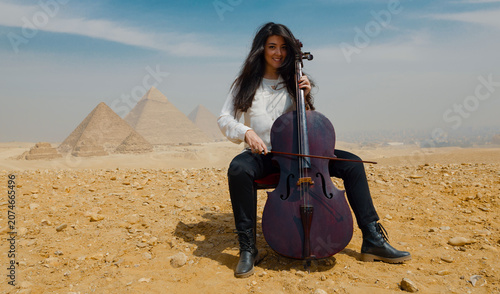 Tableau sur toile Smiling young Middle Eastern cellist playing cello in the desert before the icon